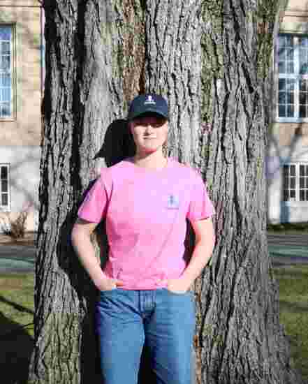Kvinnelig student med en rosa DMMH t skjorte lener seg mot et tre.
