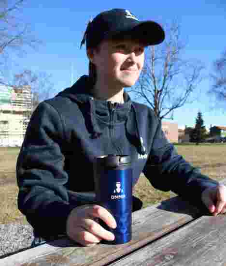 Bilde av blå DMMH termokopp som blir holdt av en student på et bord.