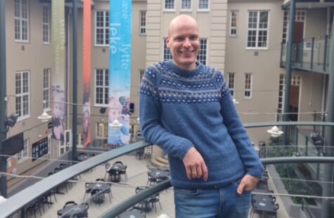 Høgskolelektor Tormod Murud-Riser lener som mot et gelender og smiler i Glassgården.